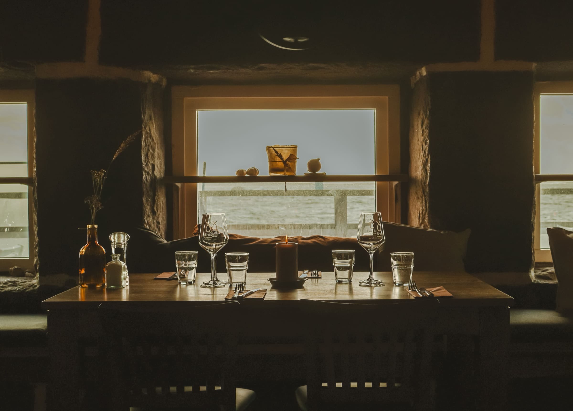 Dekket bord ved vinduet, stearinlys og havet utenfor.