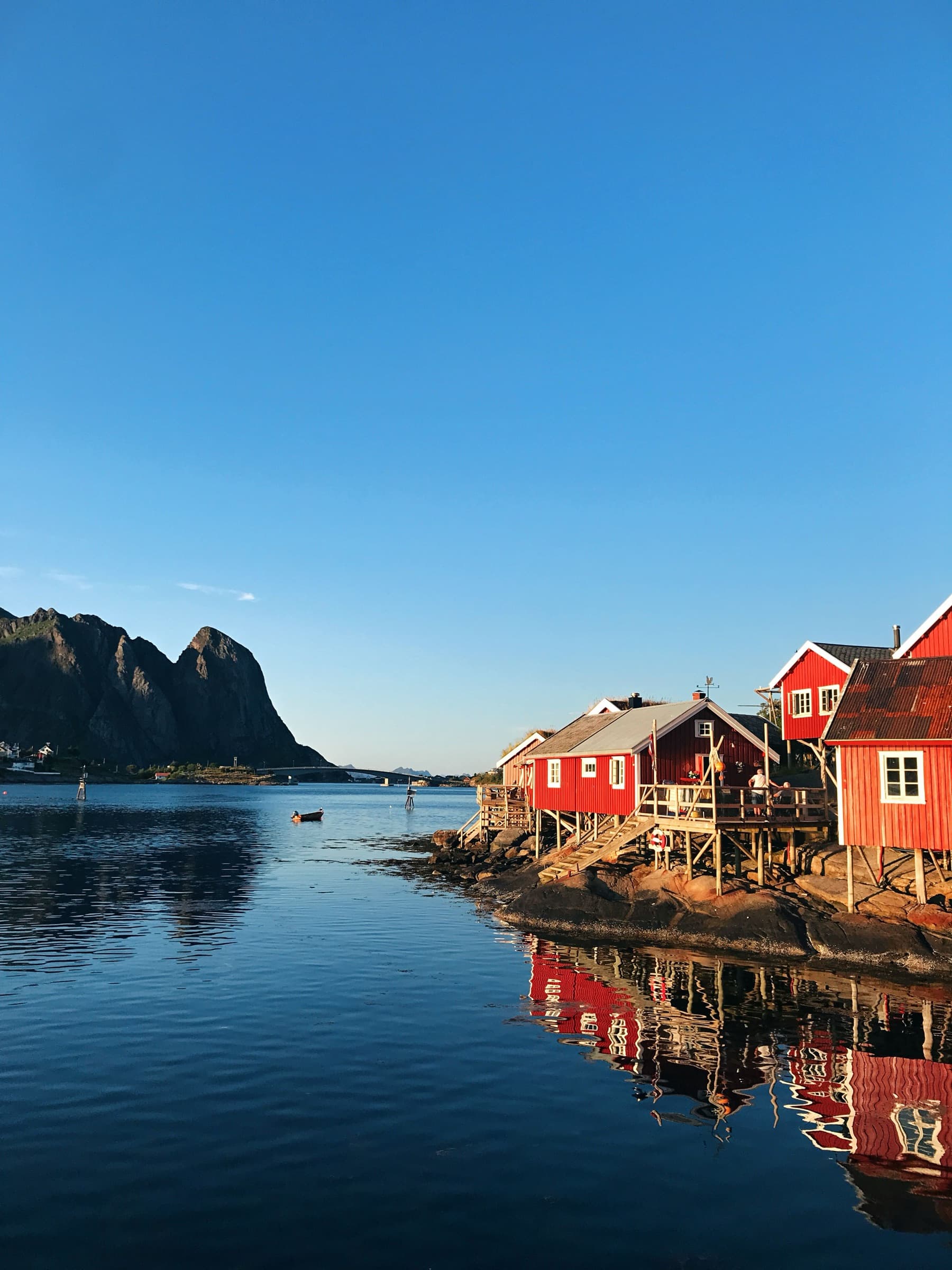 Røde rorbuer ved stille vann i Reine, lavt gyllent lys.