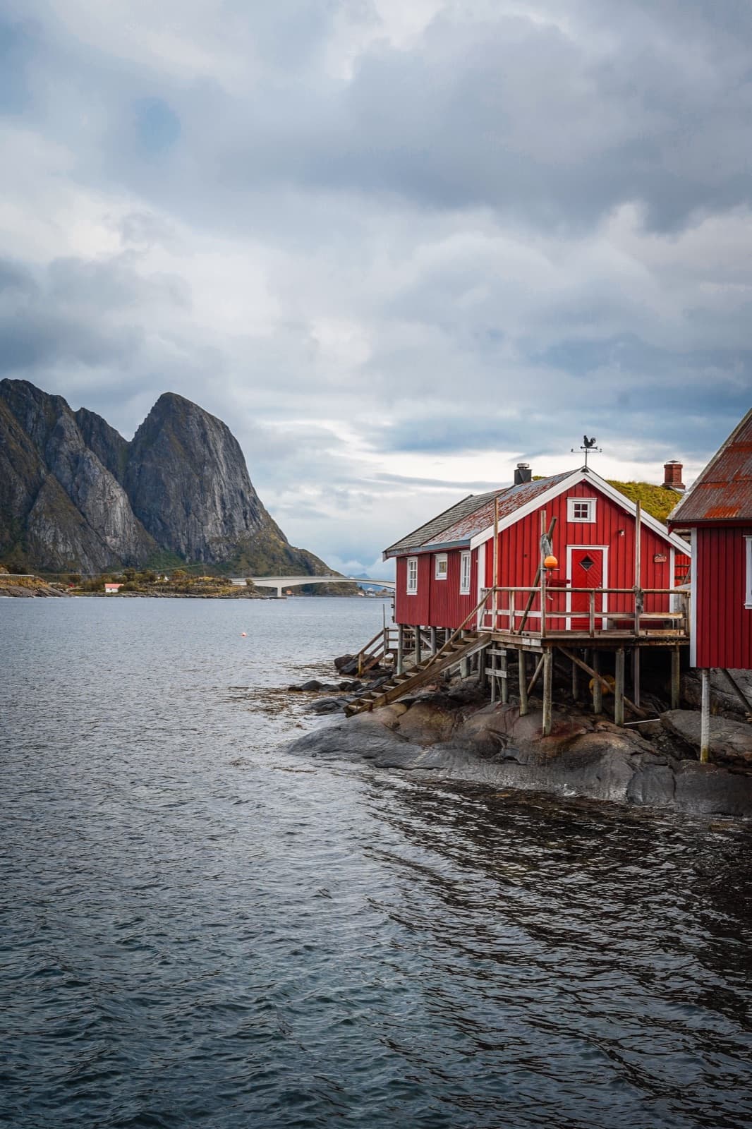 Sjøhuset: rød rorbu ytterst på berget, fjellet bak.